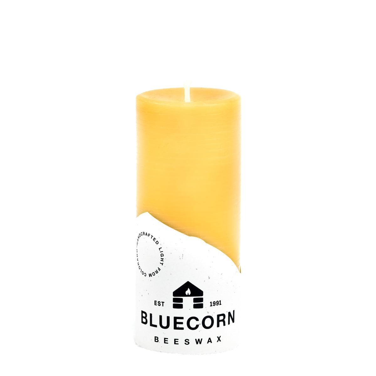 Bluecorn Candles pure beeswax pillar candles showing natural yellow wax with unburned wicks, arranged in a row on a wooden surface.