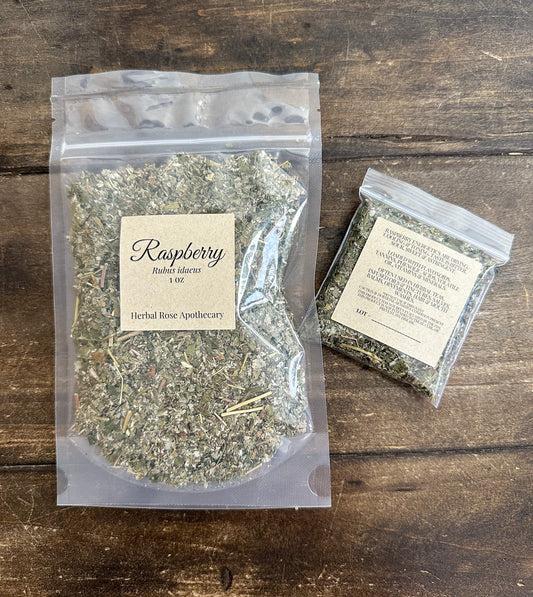 Dried raspberry leaf herbs in a clear glass jar, showing green leaves and stems, from herbalroseapothecary for herbal tea and remedies.