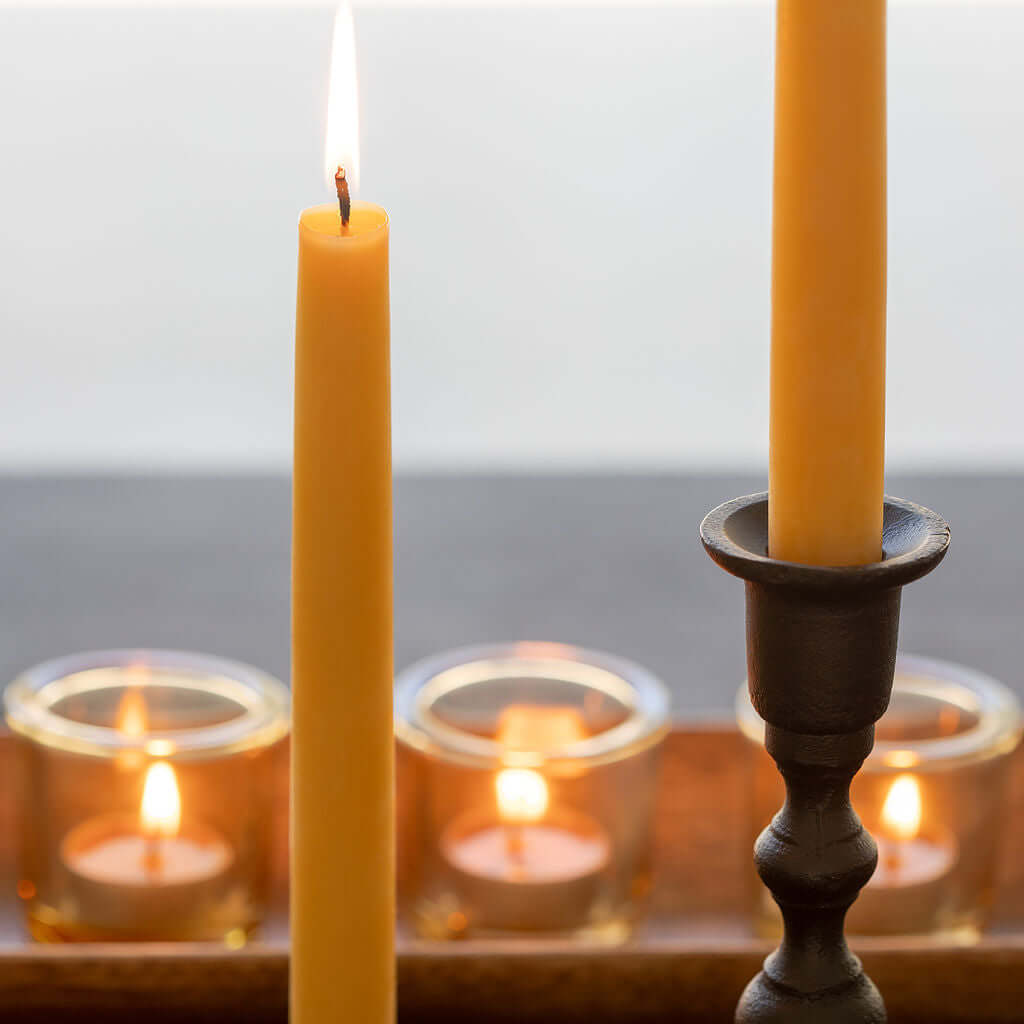 Hand-dipped beeswax taper candles from Bluecorn Candles with tea lights in the background, showing natural beeswax texture.