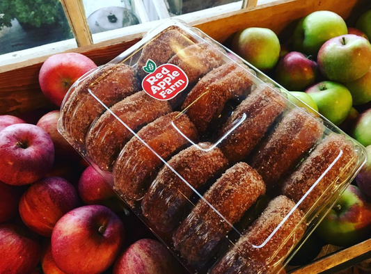 Fresh apple cider donuts from Red Apple Farm, golden-brown, coated with cinnamon sugar, and arranged on a rustic wooden surface.