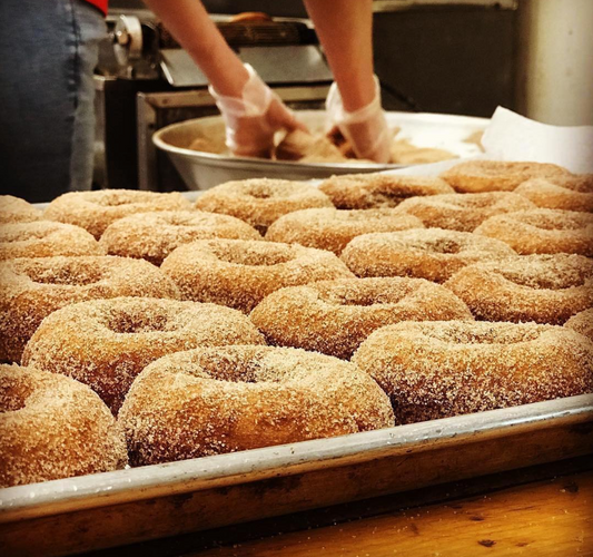 Fresh apple cider donuts from Red Apple Farm, showing golden-brown, sugared donuts on a plate with a rustic background.