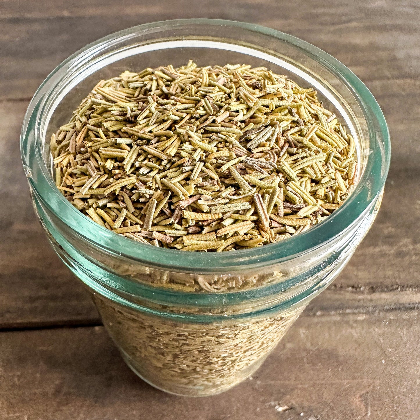 Small jar of dried rosemary herbs from HerbalRoseApothecary, showcasing a clear glass jar filled with aromatic dried rosemary