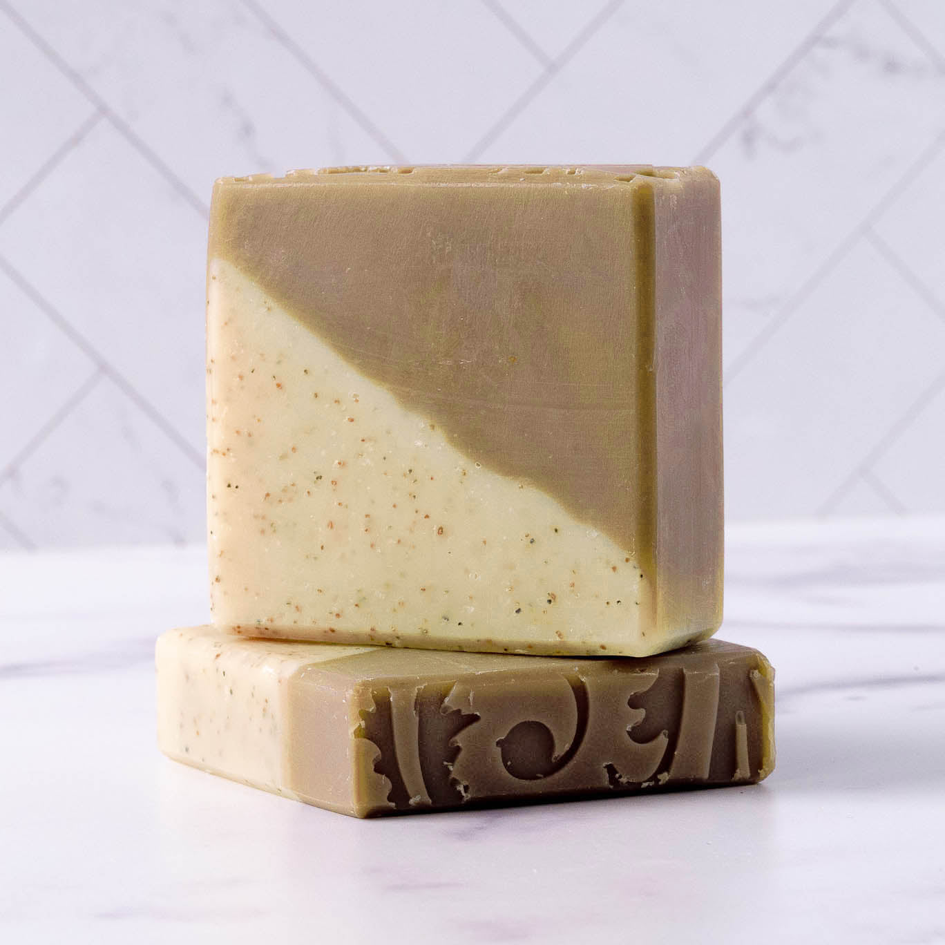 Two Rustic Strength Bar Soap | Sandalwood Patchouli bars, one upright and one flat. Each has a diagonal split of light tan and brown, hydrating natural ingredients, and a decorative swirl on the side of the bottom bar.