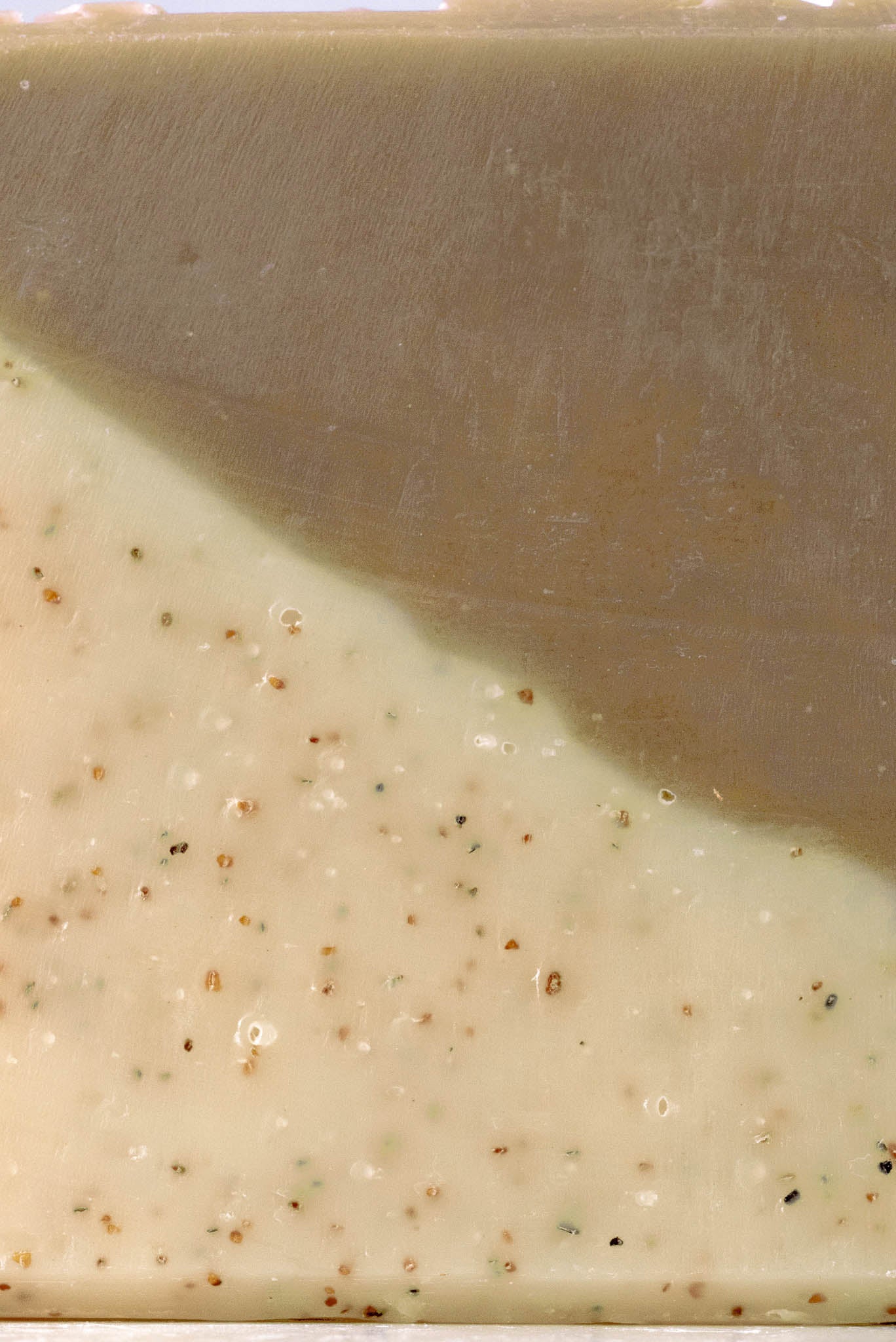 Close-up of Rustic Strengths Bar Soap | Sandalwood Patchouli: a cold process bar with a smooth beige top and a cream lower half, featuring brown and green walnut exfoliating specks.
