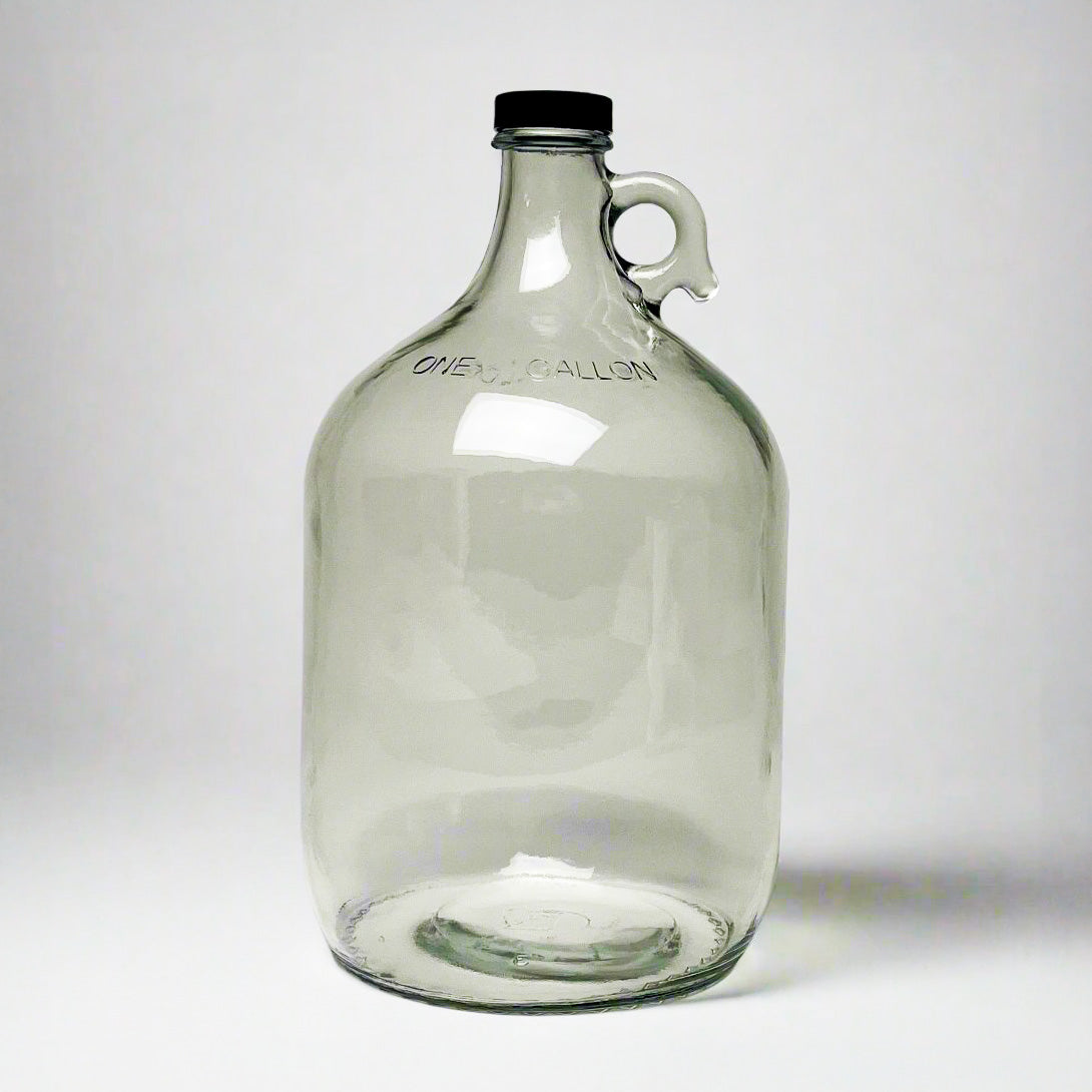 The Rustic Strength 1 Gallon Glass Jug with Cap features a clear glass body, black screw cap, small side handle, and ONE GALLON embossing near the top. Limited stock available.