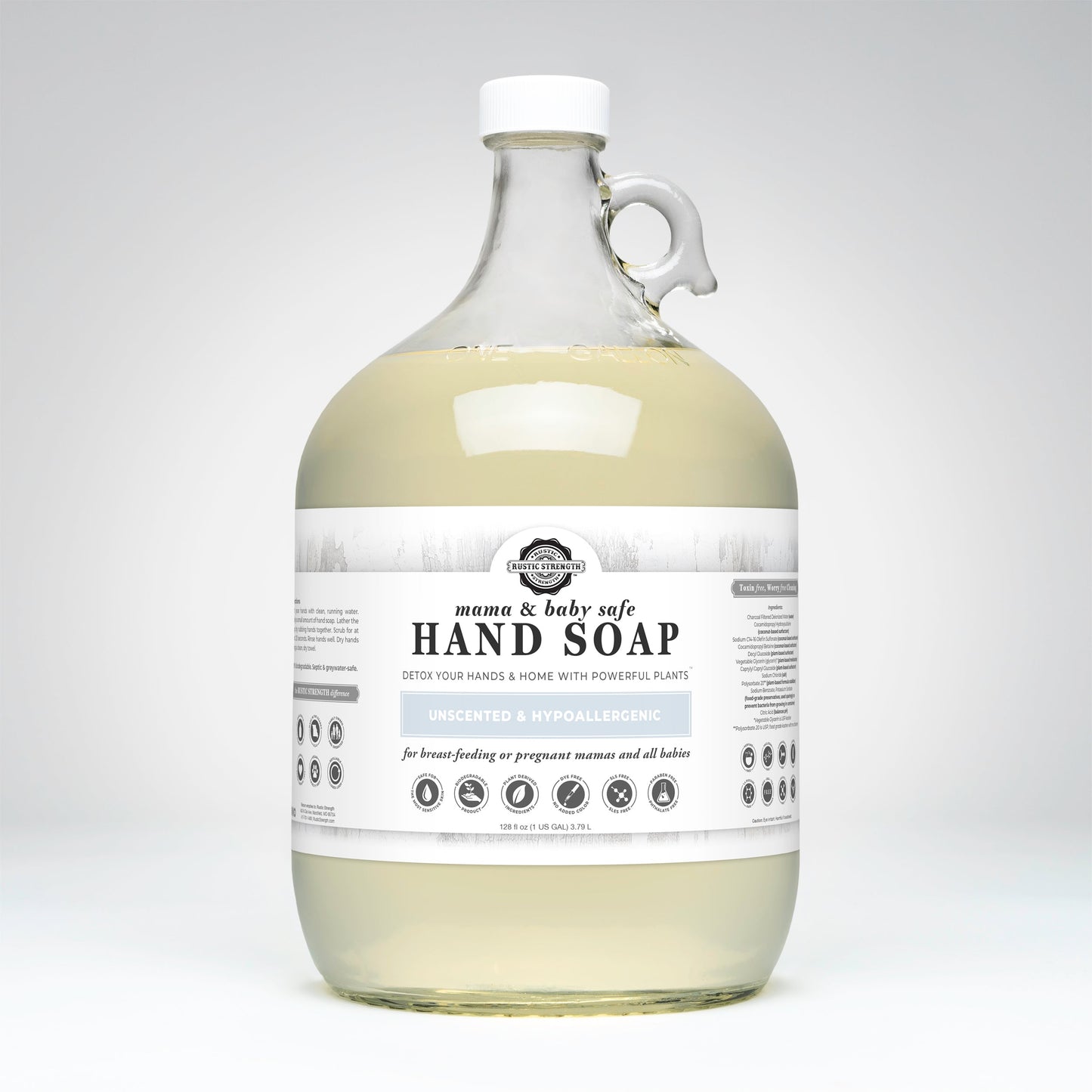 A large clear glass jug with a handle holds gentle hand soap. The white label reads Rustic Strength, Hand Soap | Mama + Baby Safe, Unscented & Hypoallergenic, with icons for safety and plant-based ingredients.