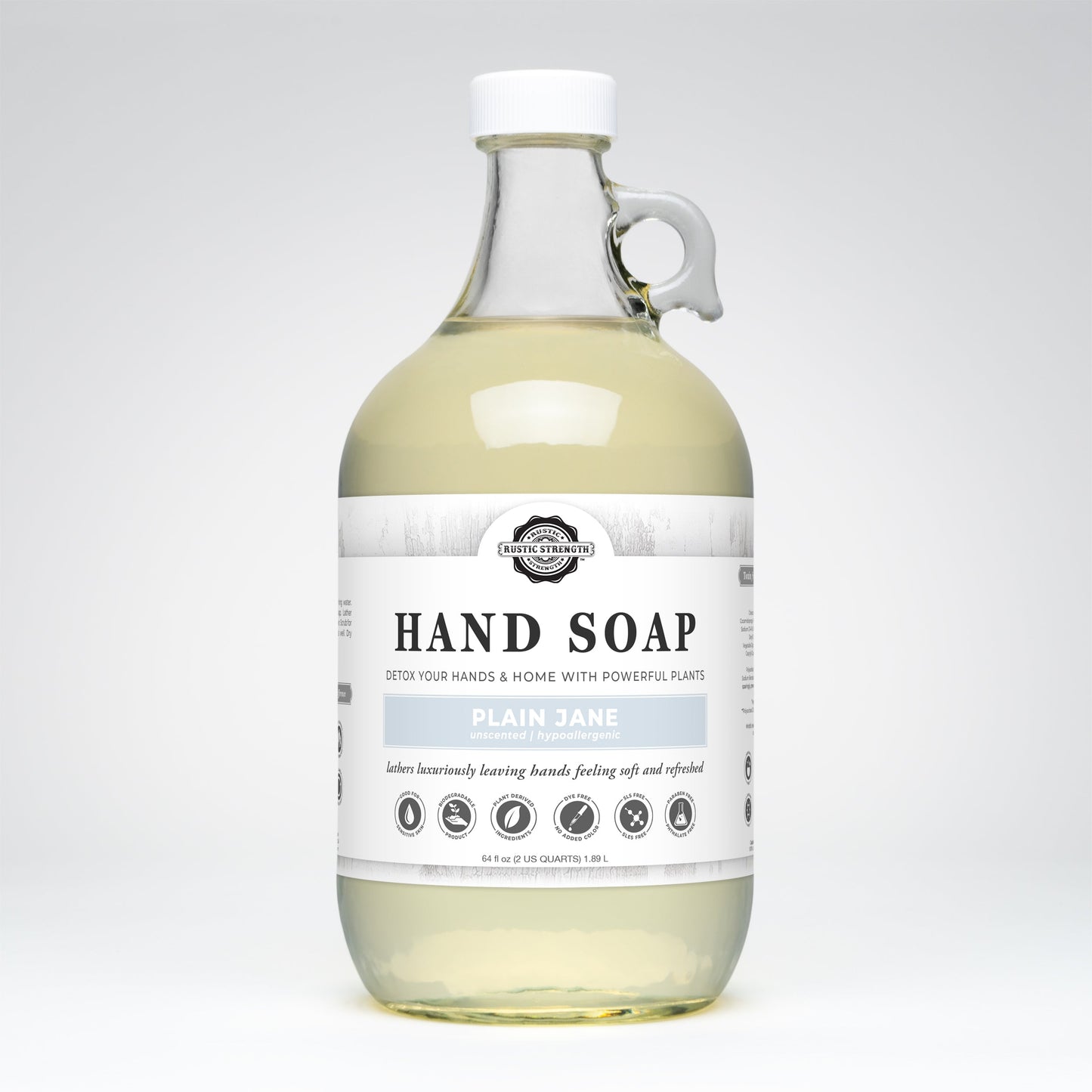 A clear bottle of Rustic Strength Hand Soap | Plain Jane features a white label highlighting sensitive skin and biodegradable icons, plus a metal neck ring and white cap.