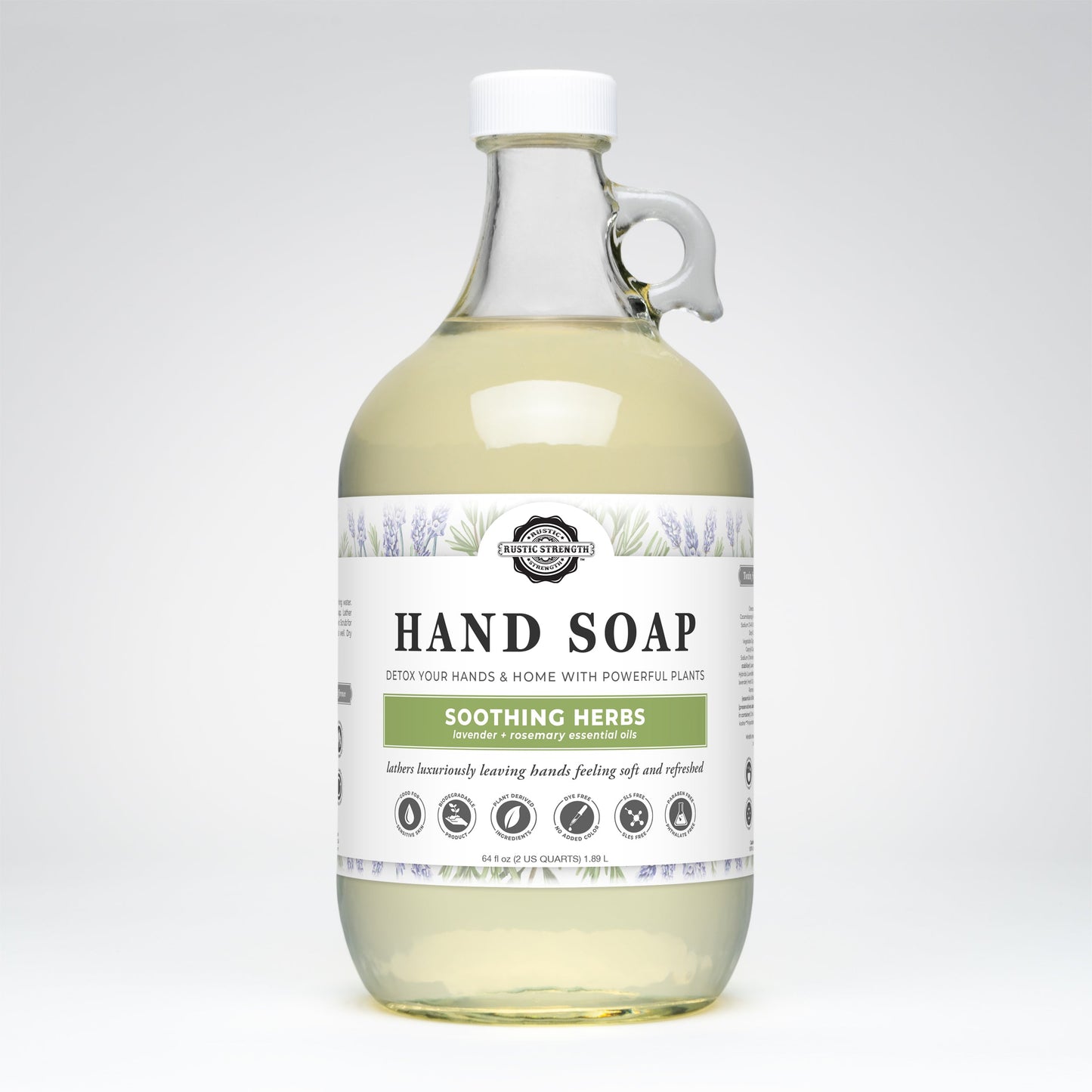 The Rustic Strength Hand Soap | Soothing Herbs comes in a clear glass bottle with a white cap and loop handle, featuring a botanical design. The light yellow soap offers a soothing lavender rosemary formula.