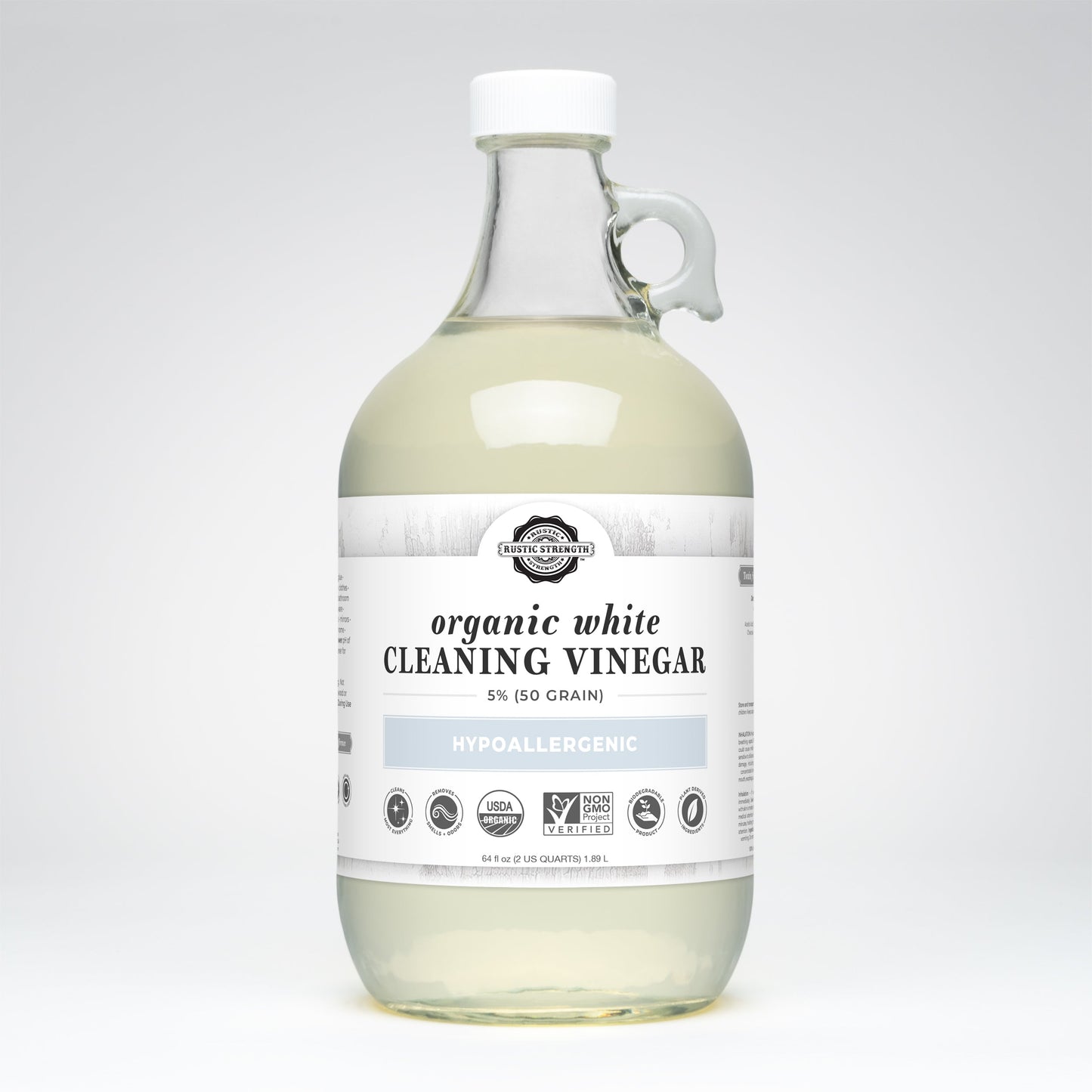 A clear glass jug with a handle contains Rustic Strength Organic White Cleaning Vinegar | 5% (50 grain). The white label reads hypoallergenic, biodegradable, Non-GMO, and USDA Organic, with certification logos displayed.