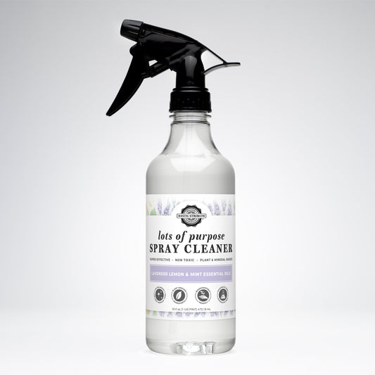 A clear spray bottle of Rustic Strength Lots of Purpose Spray Cleaner | Lavender, Lemon & Mint, with a black trigger and pastel floral label, is displayed on a plain white background.