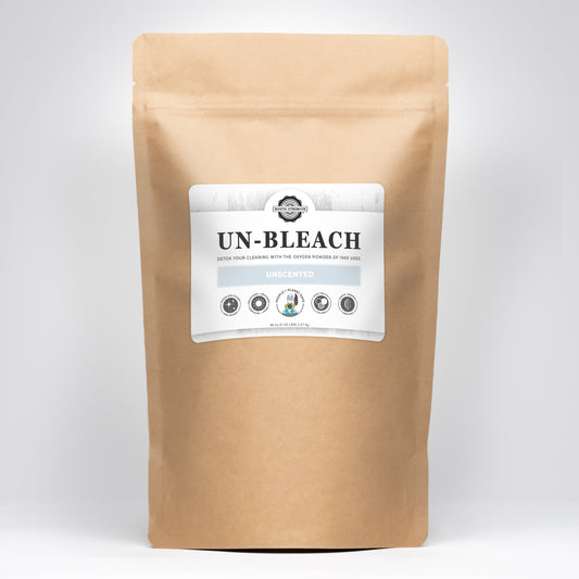 A brown paper pouch labeled Un-Bleach by Rustic Strength stands upright on a white background, featuring icons and text that highlight it as a toxin-free, unscented bleach alternative that cleans and brightens with oxygen power.