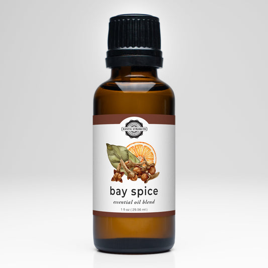 A brown glass bottle with a black cap, labeled Bay Spice Essential Oil Blend by Rustic Strength. The white label shows bay leaves, spices, and an orange slice—ideal for aromatherapy or freshening your laundry.