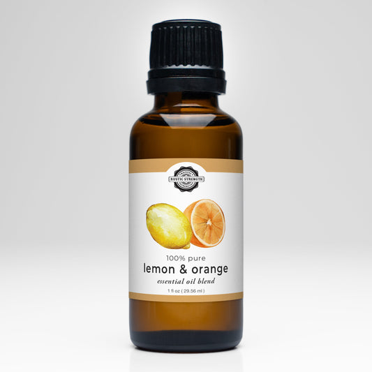 A brown bottle with a black cap displays Rustic Strength’s Lemon & Orange Essential Oil Blend. The white and gold label, adorned with citrus images, emphasizes aromatherapy benefits. The background is white.