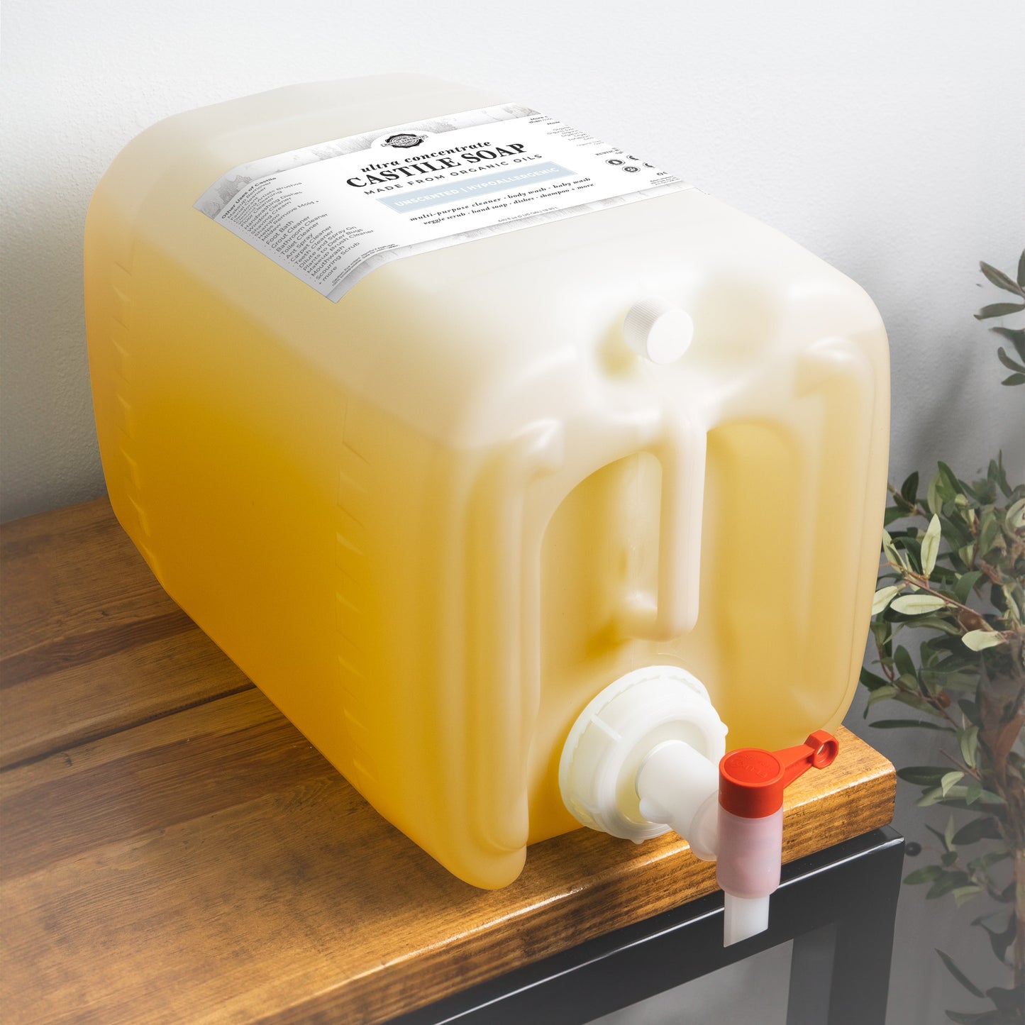 A large, translucent, rectangular plastic container of Rustic Strength Castile Soap - Ultra Concentrate | Unscented sits on a wooden surface, featuring a white twist spout with a red lever and a label detailing the product information.