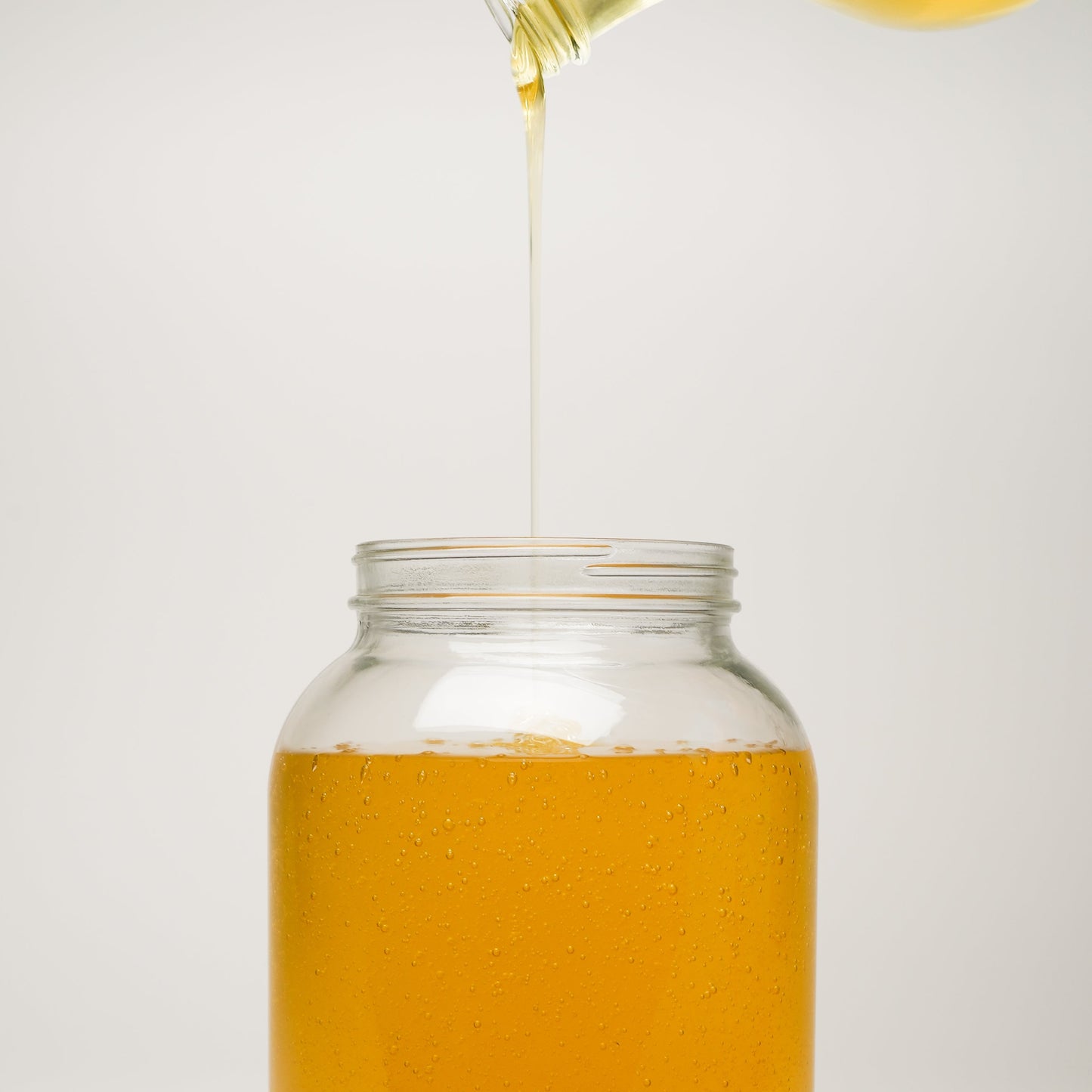 A stream of Rustic Strength Castile Soap - Ultra Concentrate | Unscented is poured from the bottle into a clear glass jar of the same soap, both set against a plain white background.