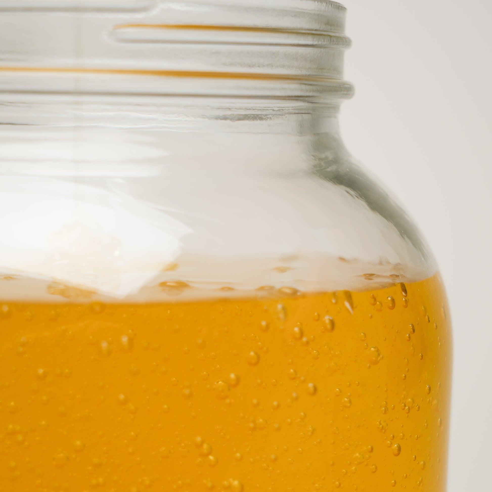 Close-up of a glass jar filled with golden honey-like liquid, evoking the natural purity of Rustic Strengths Castile Soap - Ultra Concentrate | Unscented, set partially visible against a plain, light background.