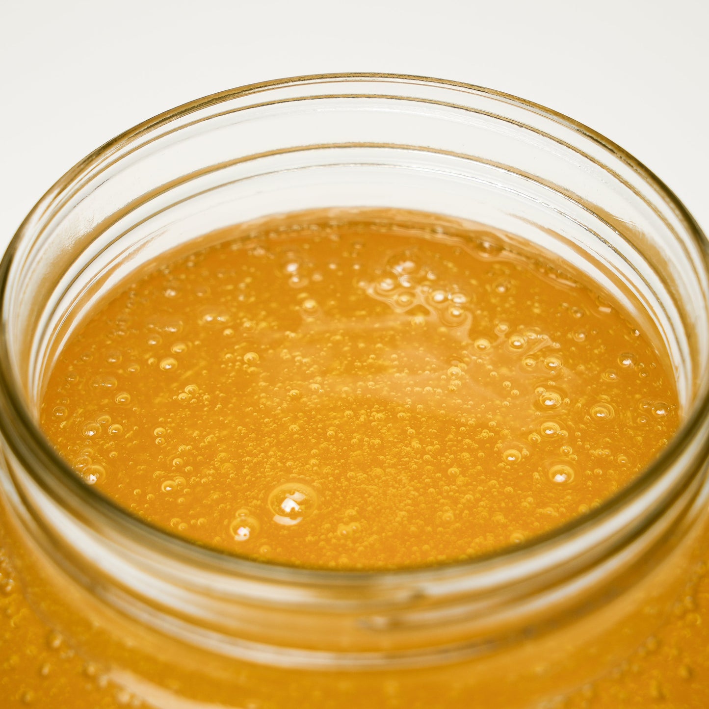 A close-up of golden honey in an open glass jar with bubbles—perfect for pairing with Rustic Strength’s Castile Soap - Ultra Concentrate | Unscented to create a gentle, multi-purpose cleaner.