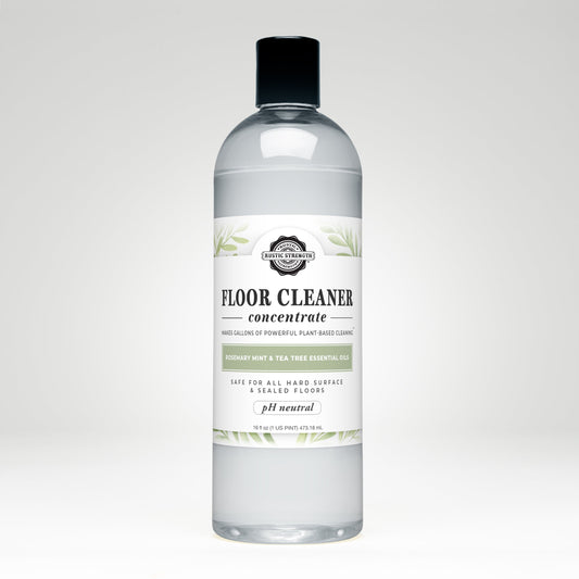 A 16.5 fl oz clear plastic bottle of Rustic Strength Floor Cleaner Concentrate | Rosemary, Mint & Tea Tree, with a black cap and a white label featuring green leaf accents and product details.
