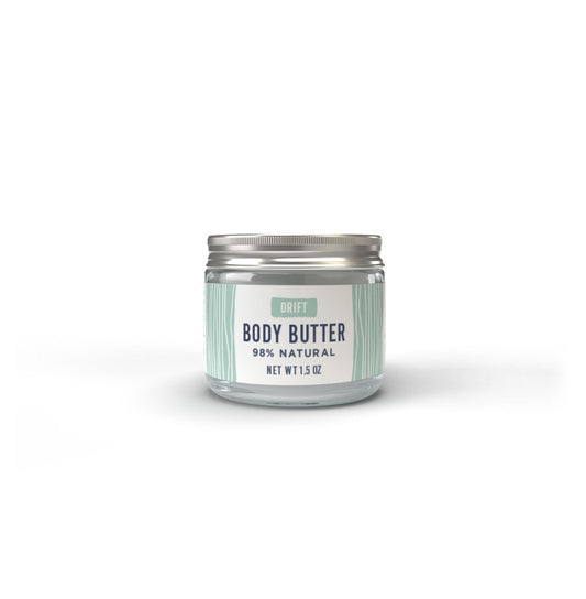 A clear jar labeled “Drift Body Butter” by Salacia Salts, with a silver lid, sits on a white background. The striped label highlights this body butter as a luxurious, natural skincare option.