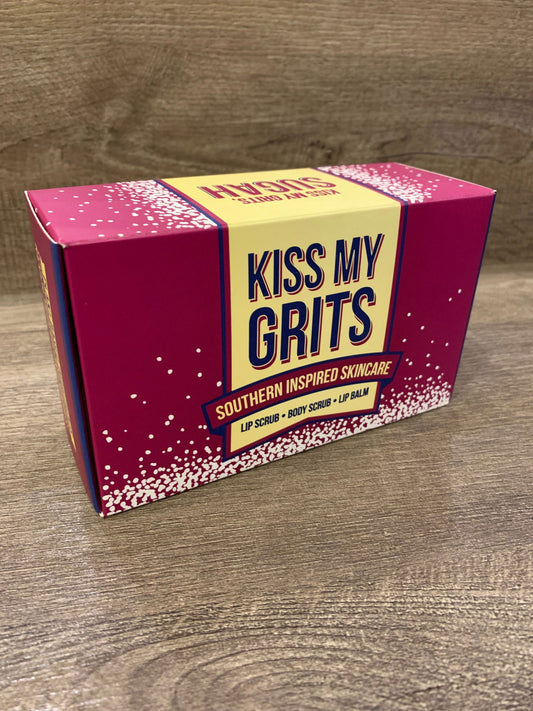 A rectangular Kiss My Grits Gift Box by Salacia Salts rests on a wooden surface. The pink and yellow speckled box features Lemon Sugah! scented body scrub, lip scrub, and classic lip balm.