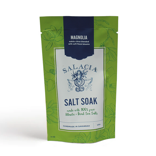 A green and white biodegradable pouch labeled Magnolia Small Salt Soak by Salacia Salts features floral designs, a mermaid logo, and highlights 100% pure Atlantic & Dead Sea salts for soothing muscle relief.