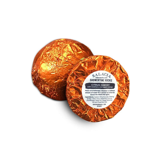 Two round aromatherapy steamers from Salacia Salts, wrapped in shiny orange foil. One is labeled ShowerTime Rocks - Citrus Convoy, showcasing its citrus aromatherapy benefits and ingredient details.