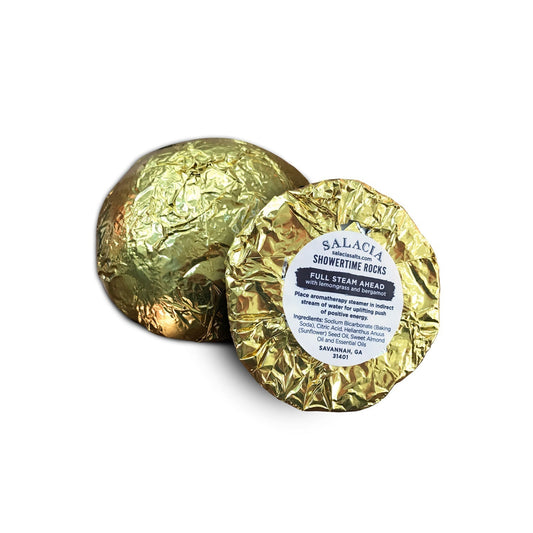 Two round ShowerTime Rocks - Full Steam Ahead shower steamers by Salacia Salts, wrapped in shiny gold foil. The label displays the product name and includes directions plus lemongrass bergamot aromatherapy ingredients.