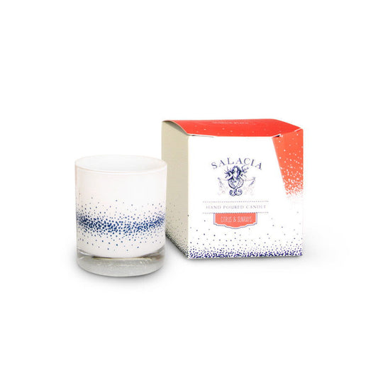 A white glass soy blend candle with blue speckles sits beside its matching box, both labeled Citrus & Sunrays Hand-Poured Candle by Salacia Salts and decorated with red and blue accents.