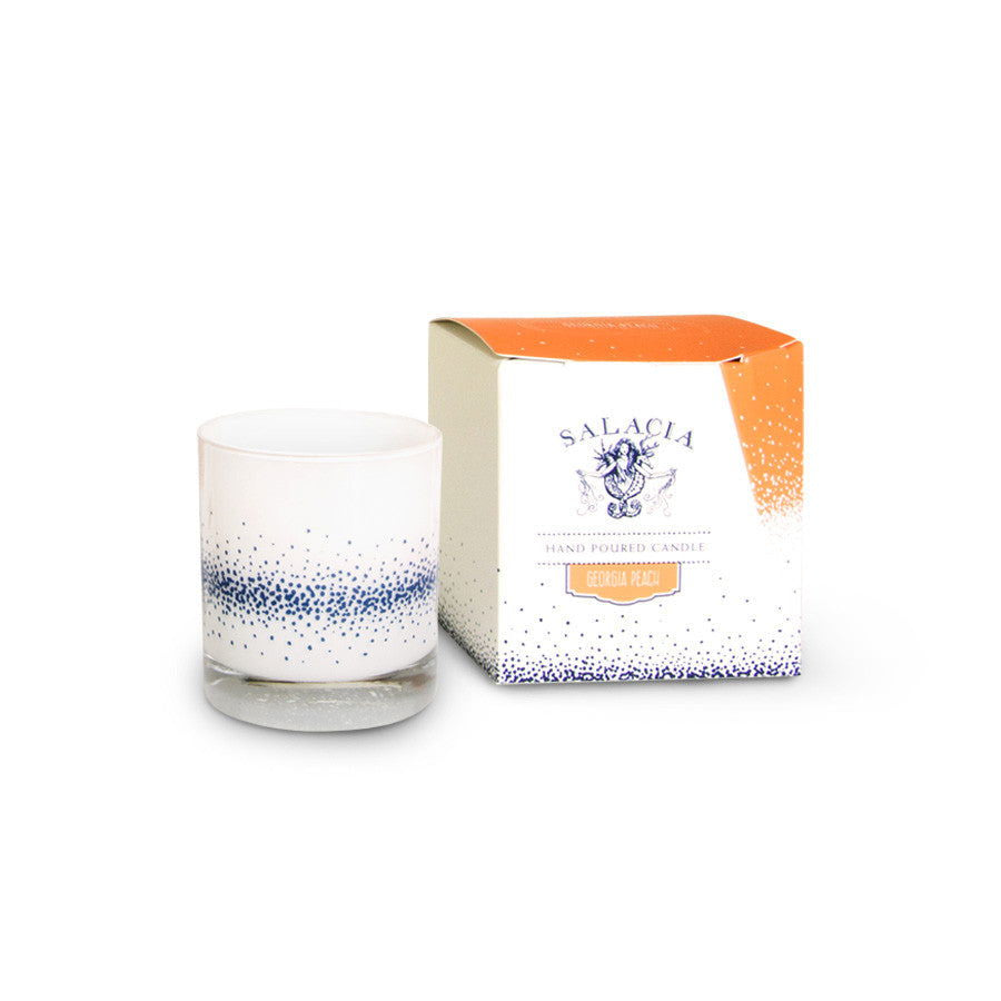 The Salacia Salts Georgia Peach Signature Candle, a hand-poured soy blend in a blue-speckled glass holder, sits beside its orange and white gradient box—an ideal Southern-inspired gift.