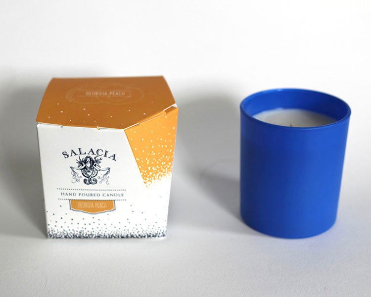 A blue hand-poured soy blend candle in a cup sits beside a white and orange box labeled “Georgia Peach Signature Candle” by Salacia Salts on a white background—the perfect Southern gift.