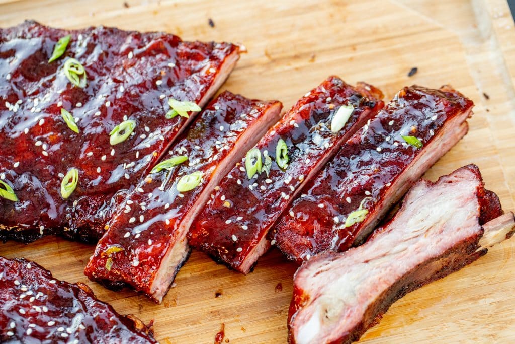 Barbecue ribs sliced on a wooden board, topped with green onions and sesame seeds, coated in SavannahSauceCompanys NEW Tangy Orange BBQ Sauce Case made from Jacksonville, Florida oranges.