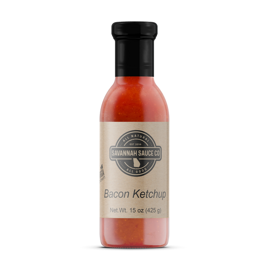 A 15 oz bottle of SavannahSauceCompany Bacon Ketchup, made with savory bacon and tomato puree, features a beige label, black cap, and the text “All Natural,” “Savannah Sauce Co,” and “Bacon Ketchup” on the front. Available in a 12 CT case.