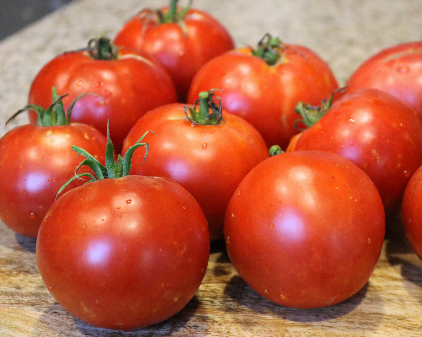 A cluster of ripe, red Burpee's Big Boy Hybrid tomatoes from Seeds 'n Such rests on a wooden surface. The large, glossy fruits with green stems and water droplets promise real tomato flavor.