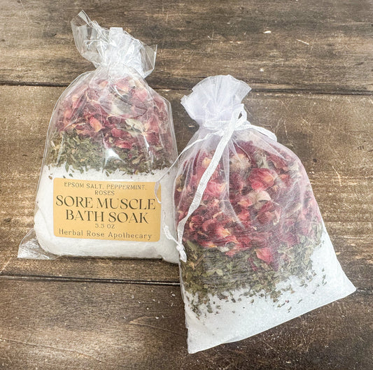Herbalroseapothecary sore muscle herbal bath soak with dried herbs and floral elements in a clear glass jar.