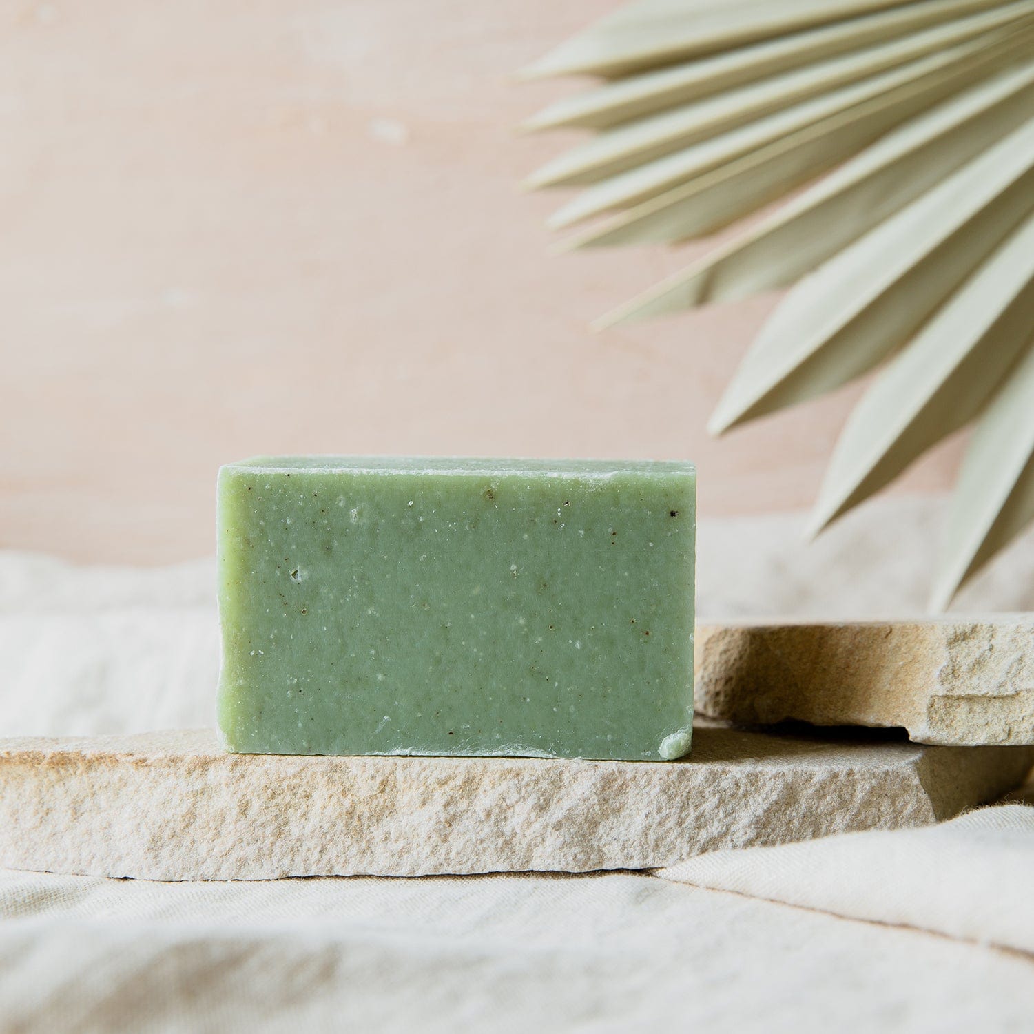 The ZeroWasteStore.com Soap Bar – 4oz, all natural and vegan with 6 scent options – rests on a light stone slab with a neutral backdrop and a dried palm leaf in the corner.