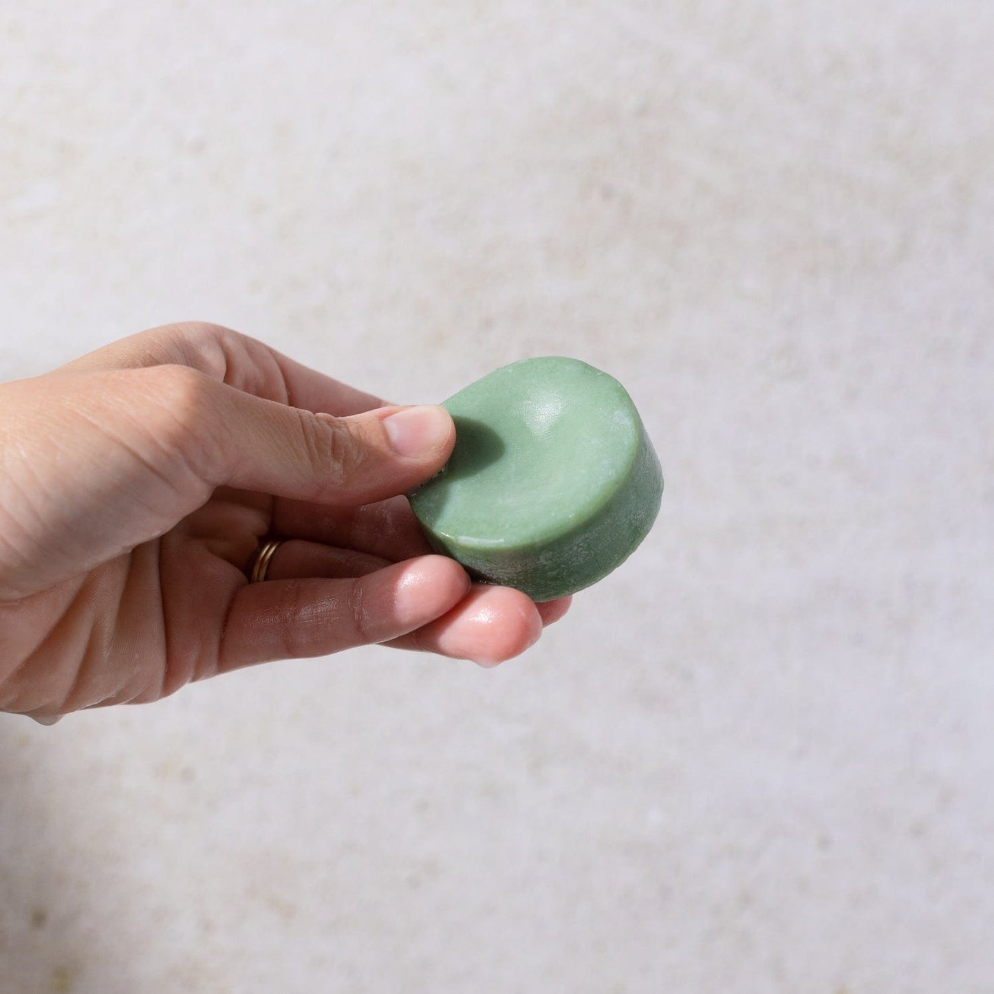 A hand holds the Bloom Castor Oil Conditioner Bar by ZeroWasteStore.com—a round, green, plastic-free hair care solution for stronger, softer, healthier hair.