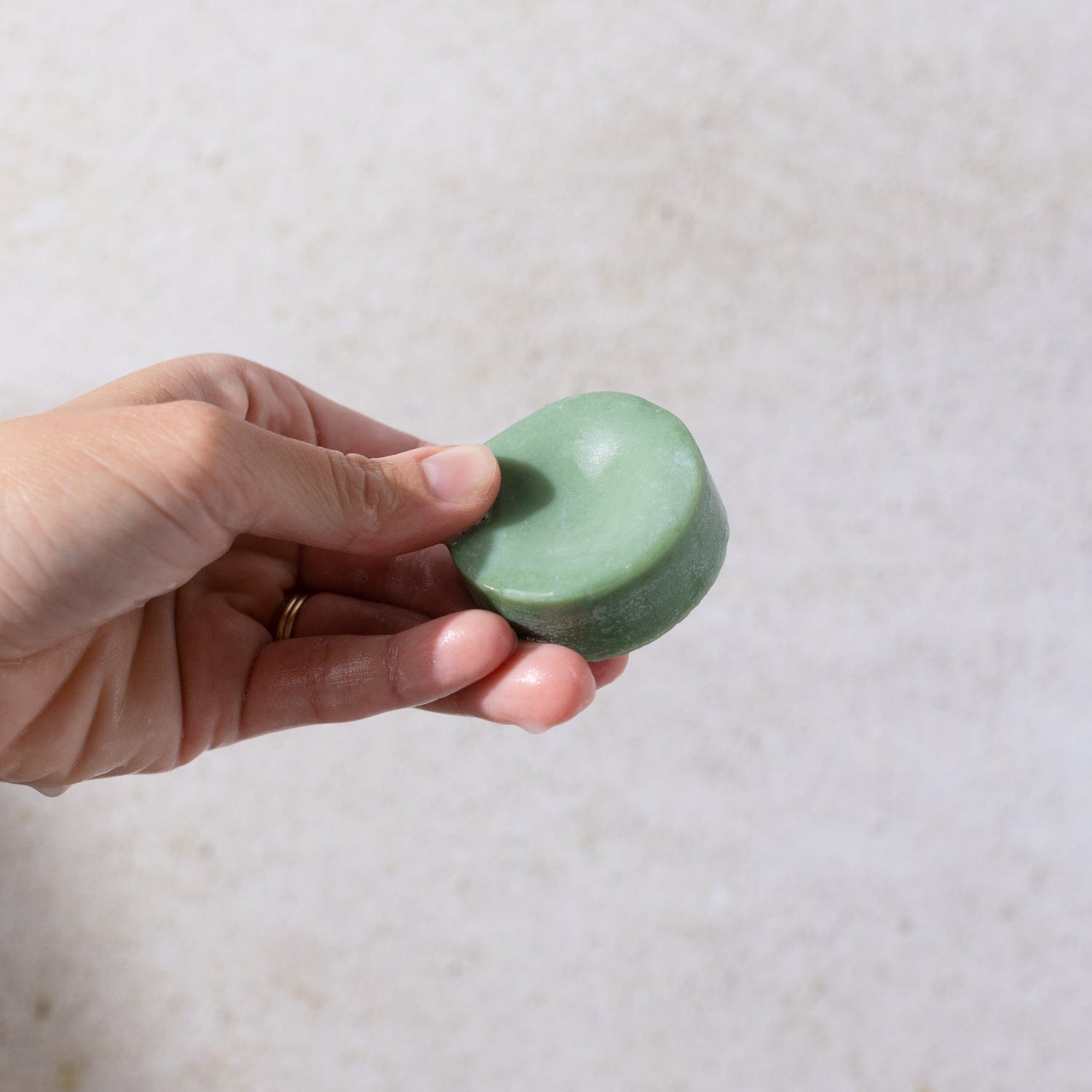 A hand holds the Bloom Castor Oil Conditioner Bar by ZeroWasteStore.com—a round, green, plastic-free hair care solution for stronger, softer, healthier hair.