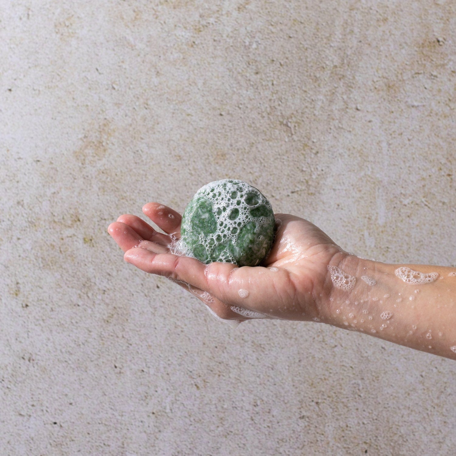 A hand holds the Bloom Castor Oil Shampoo Bar by ZeroWasteStore.com, a green, foamy, round bar—an eco-friendly, plastic-free choice for hair growth and scalp revival.