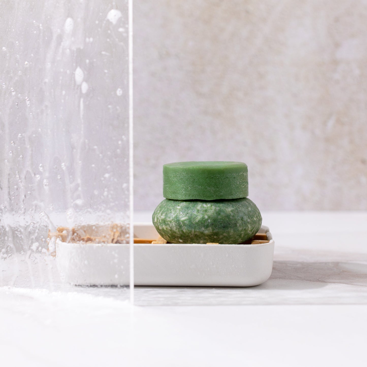 Bloom Shampoo & Conditioner Bar Duo by ZeroWasteStore.com, made with castor oil for hair growth, sits stacked on a white soap dish with water splashes nearby. The solid bars stand out against a light, neutral background.