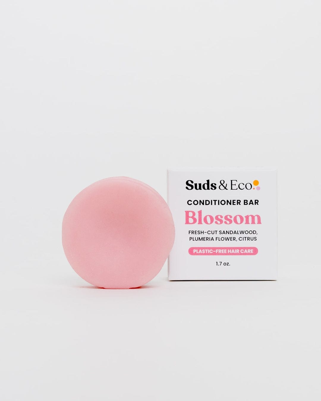 A round, pink ZeroWasteStore.com Conditioner Bar sits by a white box labeled "Conditioner Bar Blossom," featuring sandalwood, plumeria, and citrus scents. The sulfate-free bar offers plastic-free hair care.