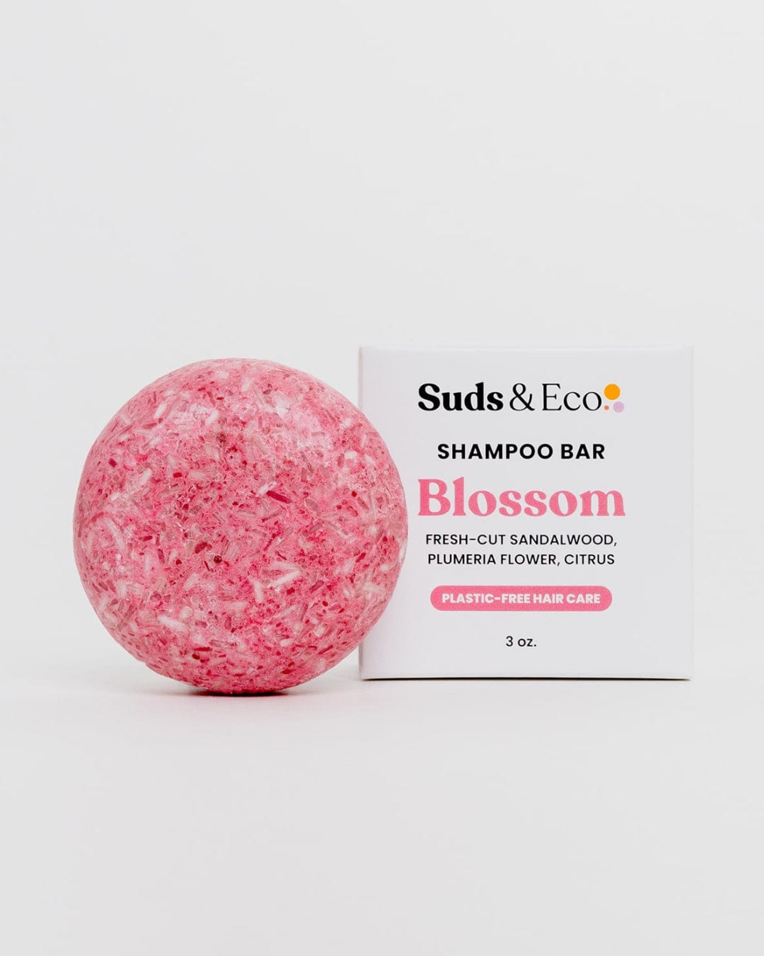 A round, pink Shampoo Bar from ZeroWasteStore.com sits beside a white box. This vegan, zero waste shampoo bar—Blossom—features sandalwood, plumeria flower, and citrus scents for plastic-free hair care.