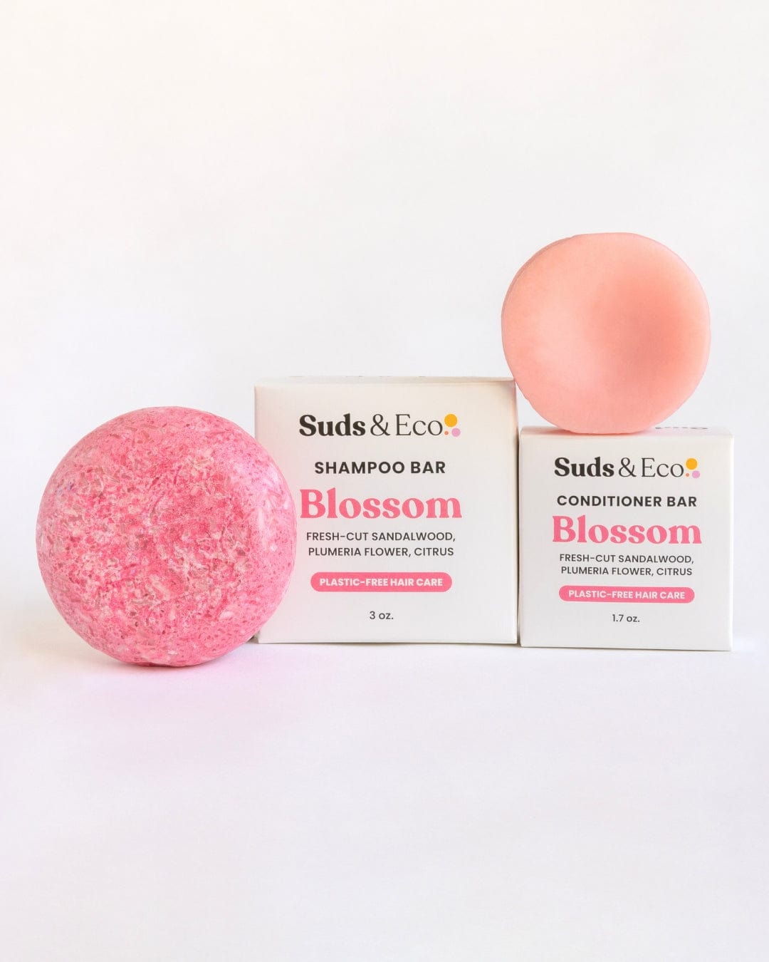 Shampoo & Conditioner Bar Duo by ZeroWasteStore.com in pink, with sandalwood, plumeria flower, and citrus scents, are displayed next to boxes highlighting their zero waste, plastic-free hair care benefits.