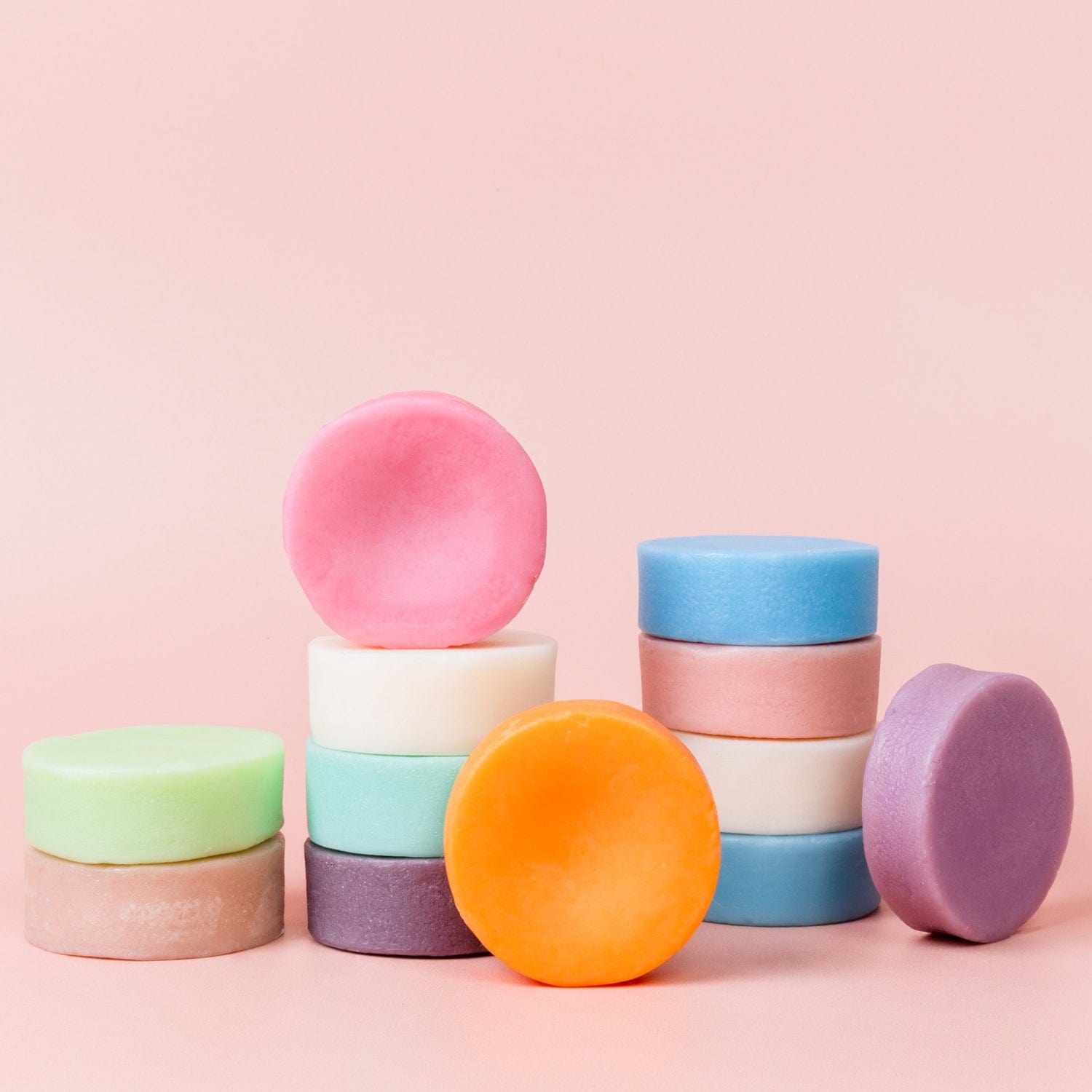 ZeroWasteStore.com Conditioner Bars, sulfate-free and available in pastel and vibrant hues like pink, green, orange, blue, purple, and white, are stacked on a light pink background—ideal for a zero waste hair care routine.