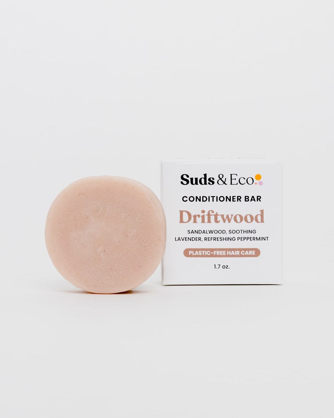A round, peach-colored sulfate-free Conditioner Bar from ZeroWasteStore.com sits by a white box labeled "Conditioner Bar Driftwood" with sandalwood, lavender, and peppermint scents. The 1.7 oz box states it's zero waste.