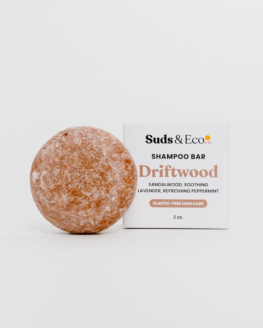 A round, brown Shampoo Bar by ZeroWasteStore.com sits beside its box labeled "Shampoo Bar Driftwood" with sandalwood, lavender, and peppermint scents. The 3 oz vegan bar offers zero-waste, plastic-free hair care.