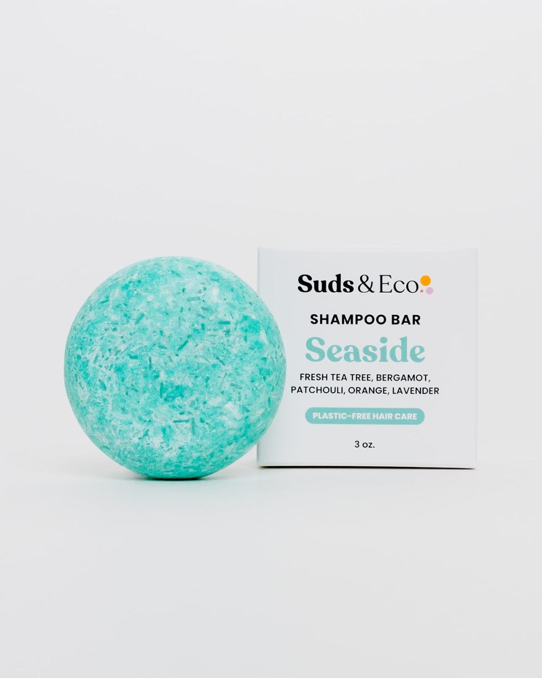 A round, turquoise Shampoo Bar from ZeroWasteStore.com sits next to its white box. Infused with tea tree, bergamot, patchouli, orange, and lavender for a zero waste shampoo experience.