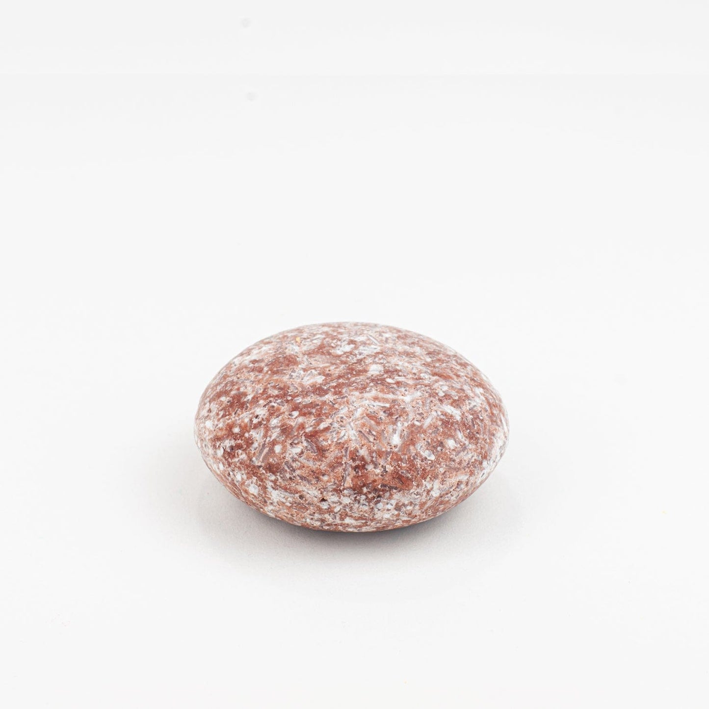 A round, smooth reddish-brown Shampoo Bar by ZeroWasteStore.com with white speckles rests on a plain white background.
