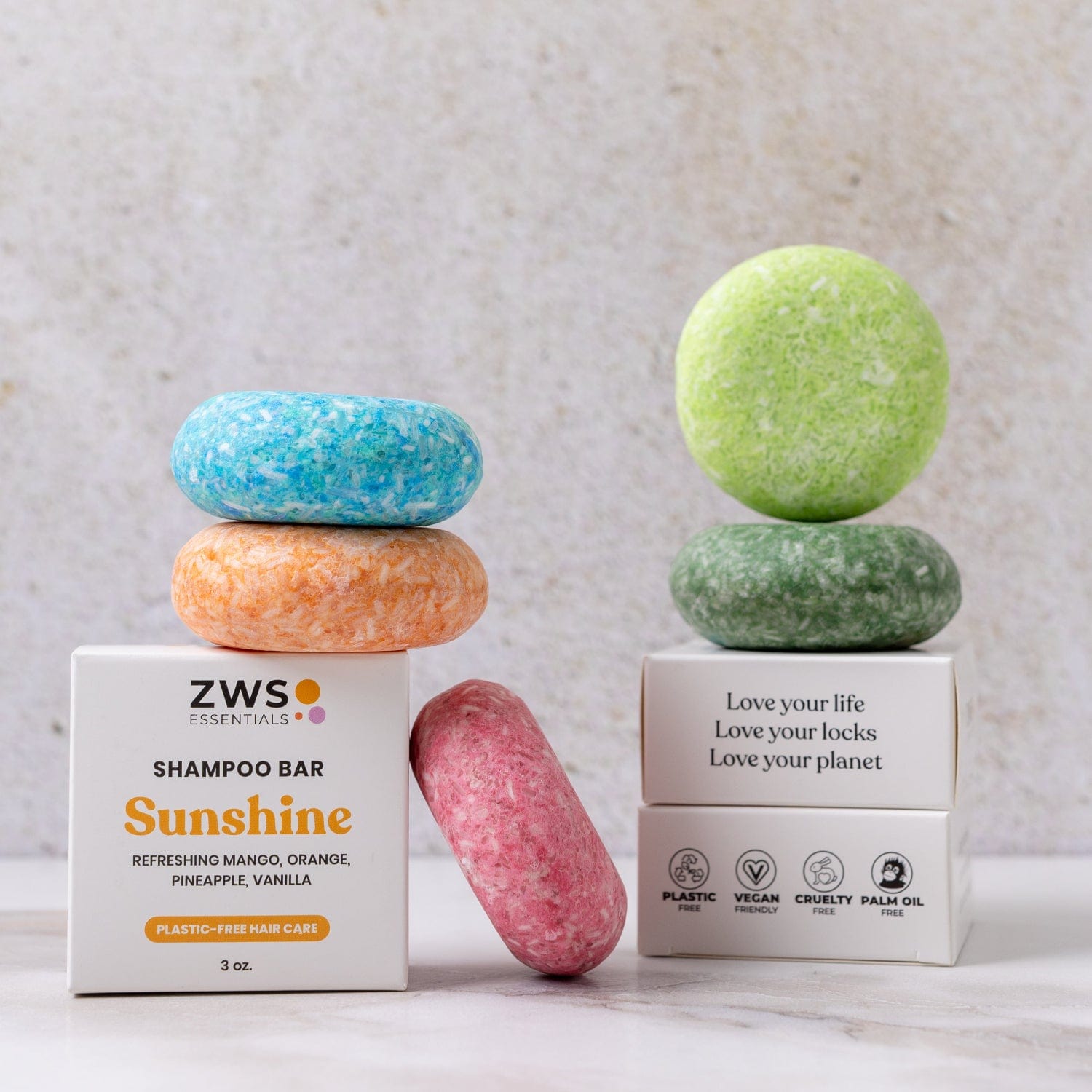 Four colorful Shampoo Bars by ZeroWasteStore.com (blue, orange, pink, green) are stacked on two white boxes with branded labels and eco-friendly icons, set against a light, textured background.