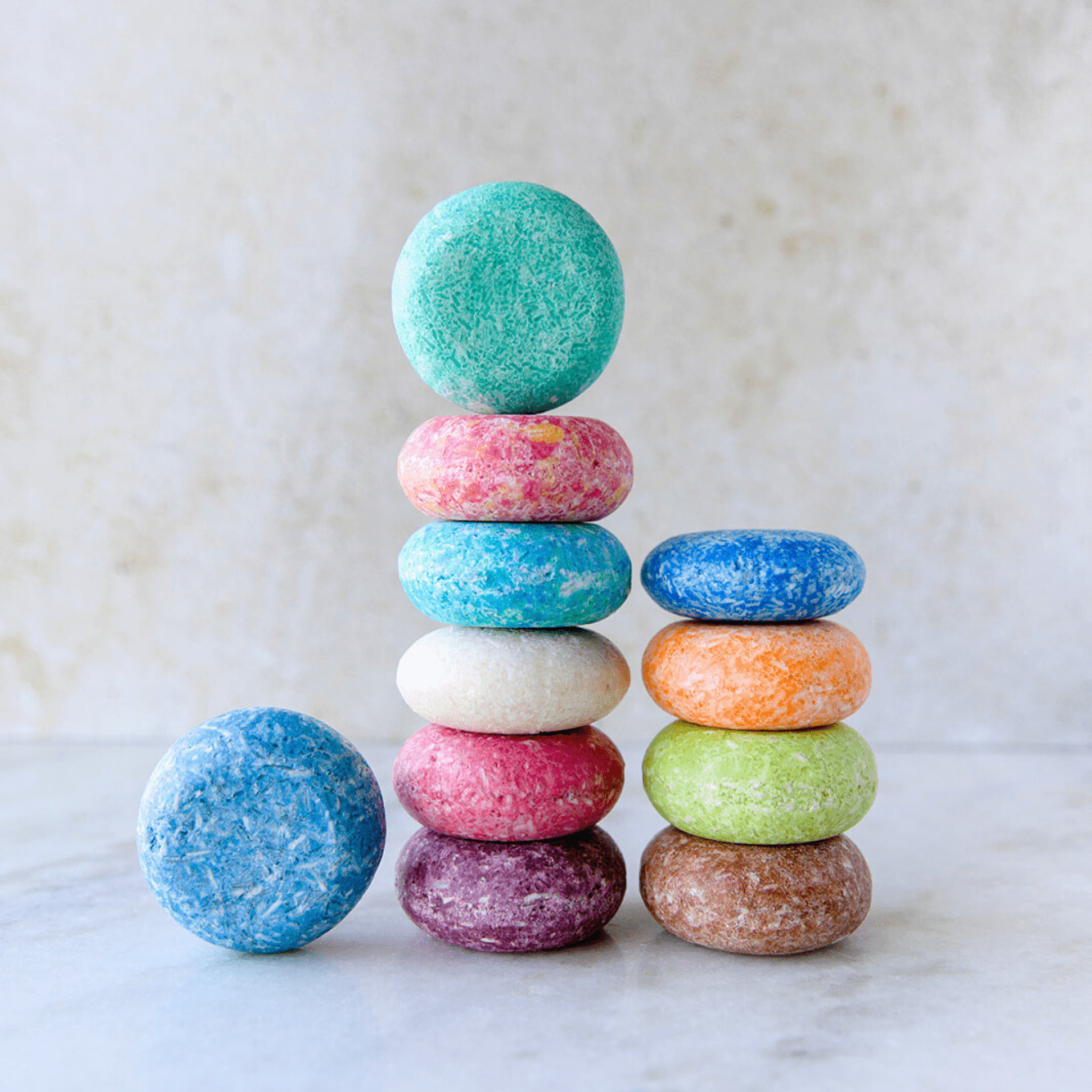 A vibrant stack of round Shampoo Bars from ZeroWasteStore.com, featuring a blue bar leaning on the stack, highlights the colorful Zero Waste Shampoo against a light, neutral background.