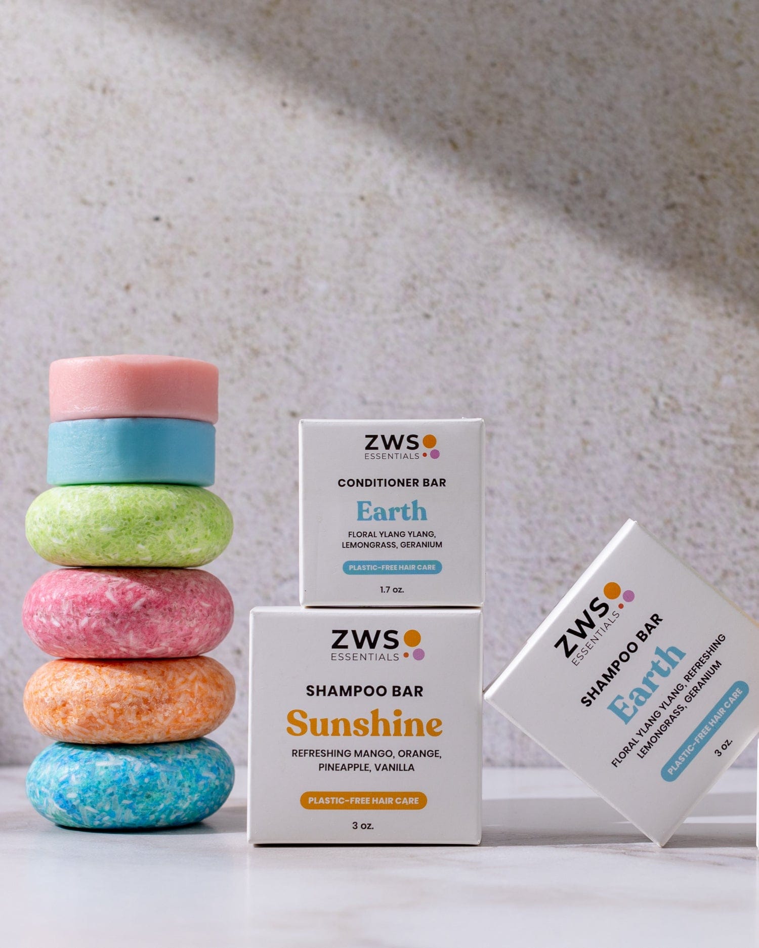 Four colorful Shampoo & Conditioner Bar Duo bars from ZeroWasteStore.com are stacked on the left as a zero waste solution, while three white ZWS Essentials boxes labeled Sunshine and Earth stand upright and angled on the right against a light background.